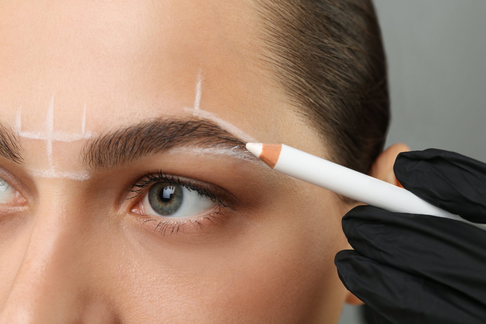 beautician-preparing-young-woman-procedure-permanent-eyebrow-makeup-grey-background-closeup
